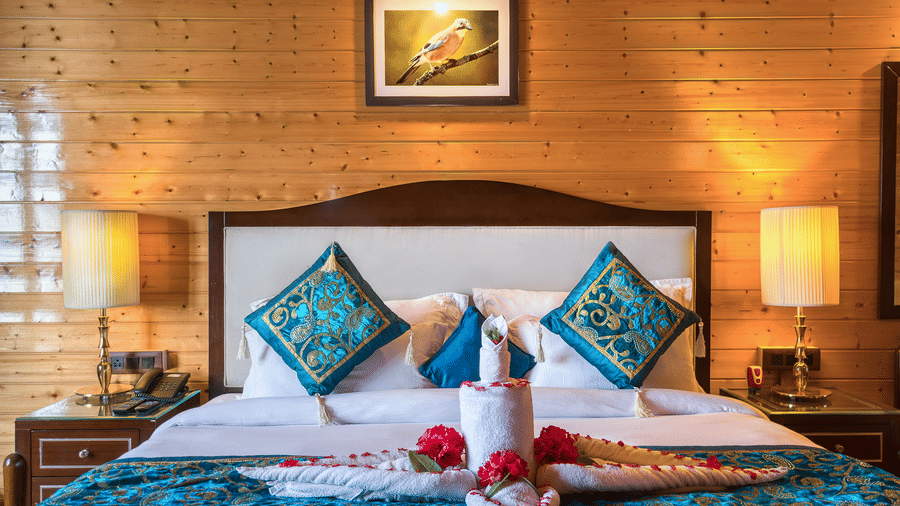 A serene bedroom at Digantaa Resorts in Mukteshwar wooden walls and a large bed adorned with bedding, featuring a red rose on a tray 